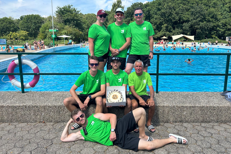 Gruppe in grünen T-Shirts mit einer 50-Jahre-Torte vor dem Becken des Freibads Selbachpark