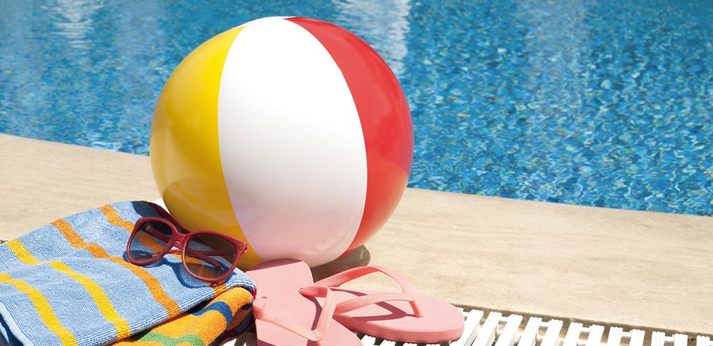 Am Beckenrand liegen ein Wasserball, Handtücher und Flipflops