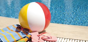 Am Beckenrand liegen ein Wasserball, Handtücher und Flipflops